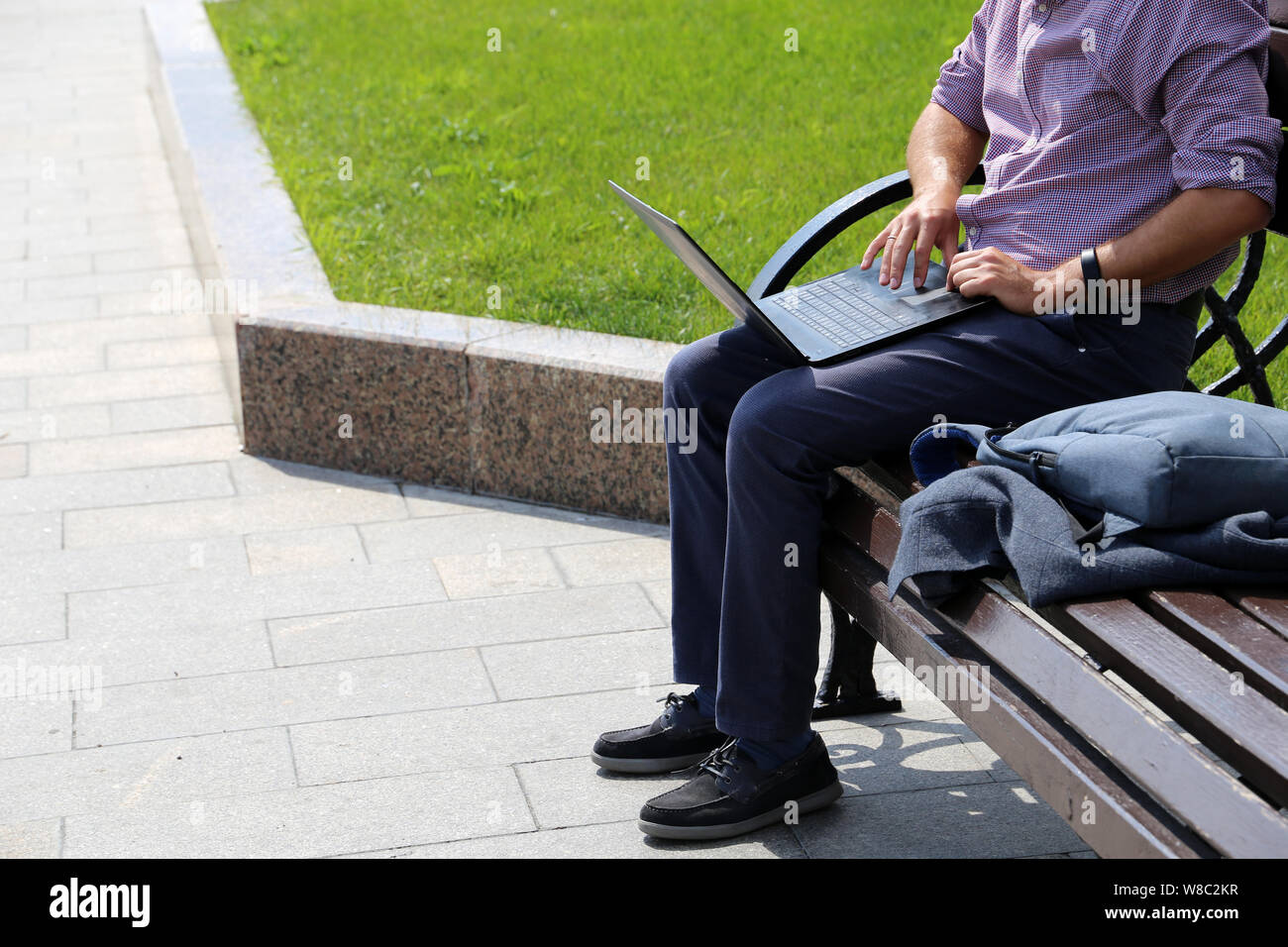 Homme assis avec un ordinateur portable sur un banc dans une ville d'été sur la pelouse verte. Les mains des hommes sur un clavier, concept d'affaires, piscine de travail Banque D'Images