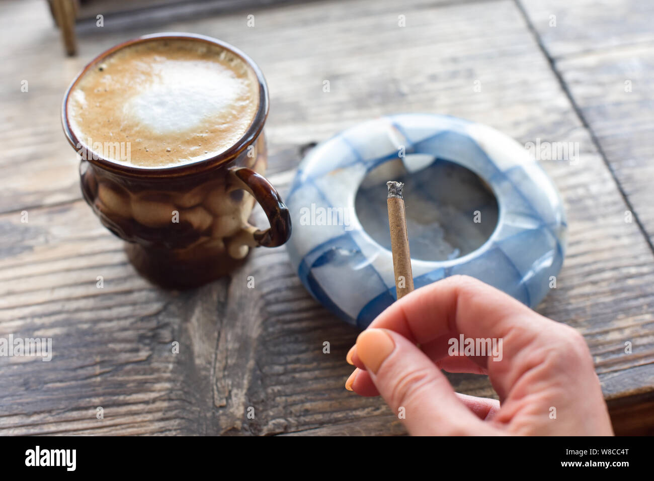 Cigarette café sur la table. Cigarette à la main d'une femme avec une belle manucure. Cendrier bleu. La fumée de cigarettes. Brown tasse avec du café sur Banque D'Images