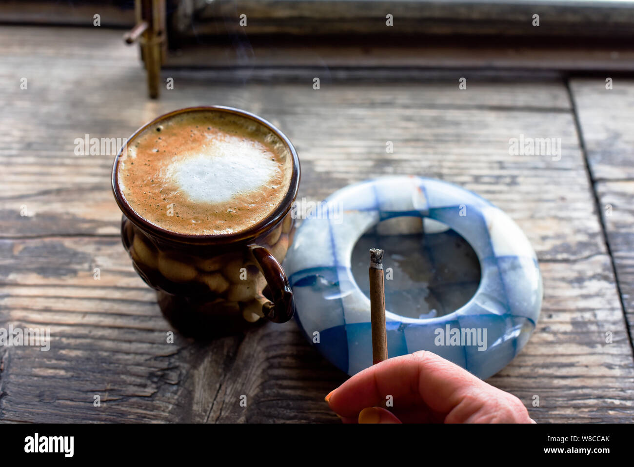 Cigarette café sur la table. Cigarette à la main d'une femme avec une belle manucure. Cendrier bleu. La fumée de cigarettes. Brown tasse avec du café sur Banque D'Images