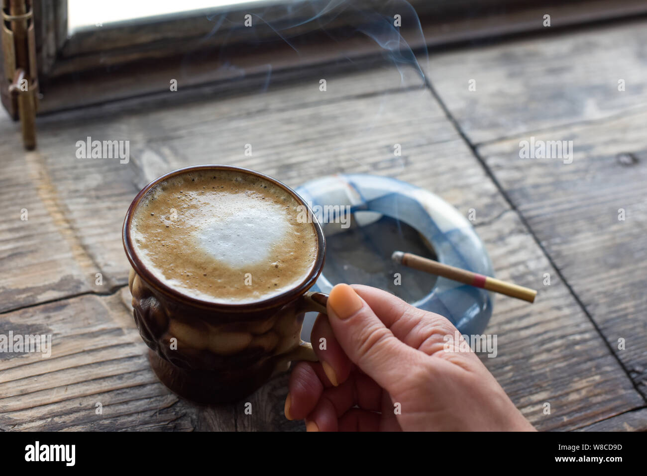 Cigarette café sur la table. Cigarette à la main d'une femme avec une belle manucure. Cendrier bleu. La fumée de cigarettes. Brown tasse avec du café sur Banque D'Images