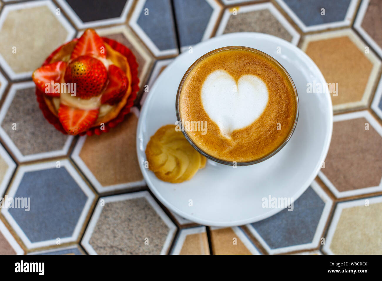 Un verre de café au lait et une tarte aux fraises sur une table en céramique colorée dans un café. Banque D'Images
