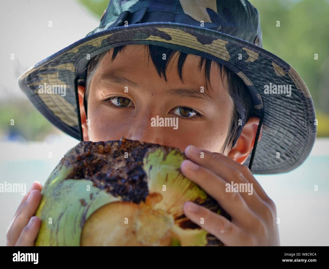Cute little boy de race mixte (Caucase et Asie du sud-est de l'eau de coco) Boissons à partir d'une noix de coco fraîche. Banque D'Images