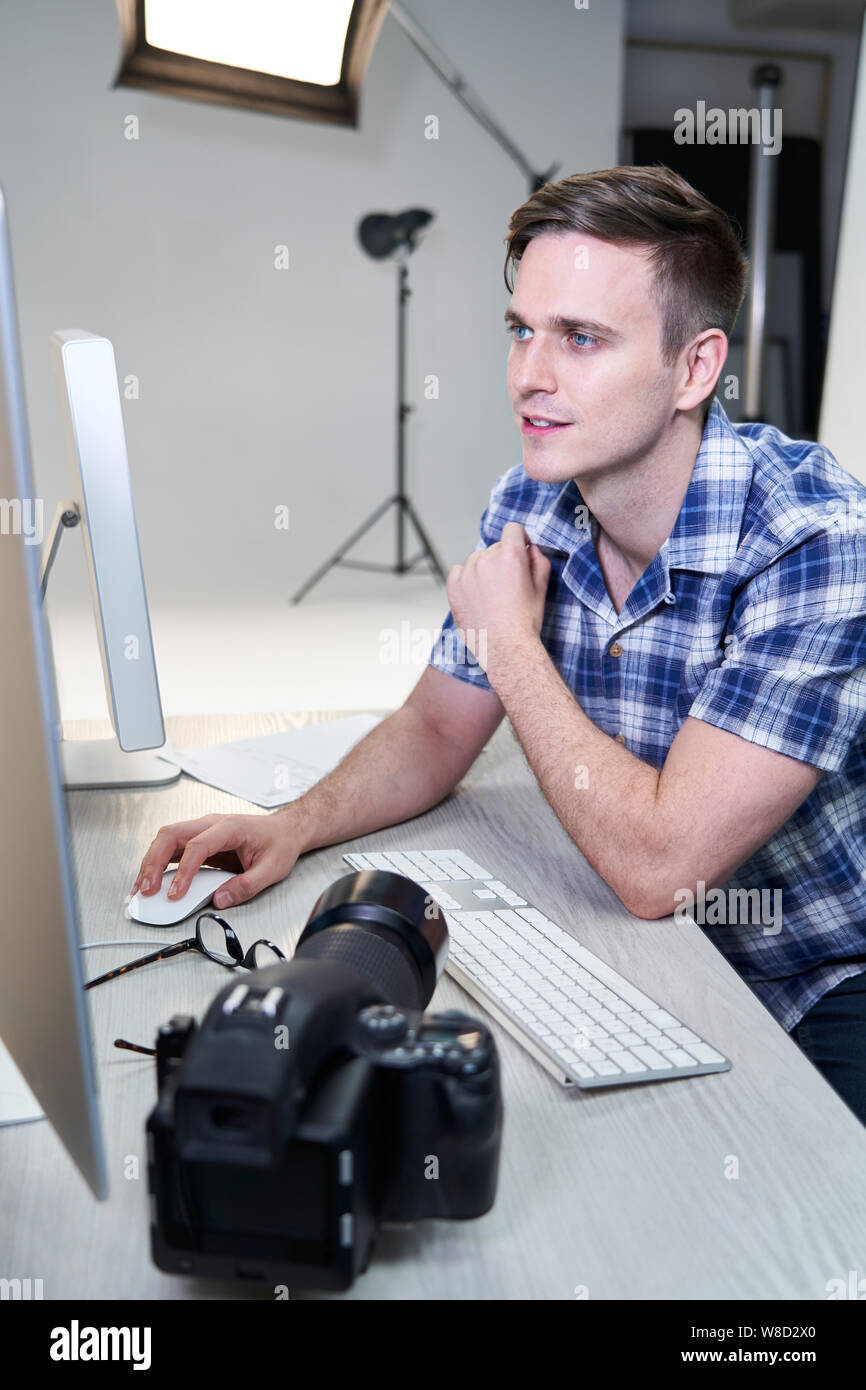 Homme Photographe en studio l'examen des images de la séance photo sur l'ordinateur Banque D'Images