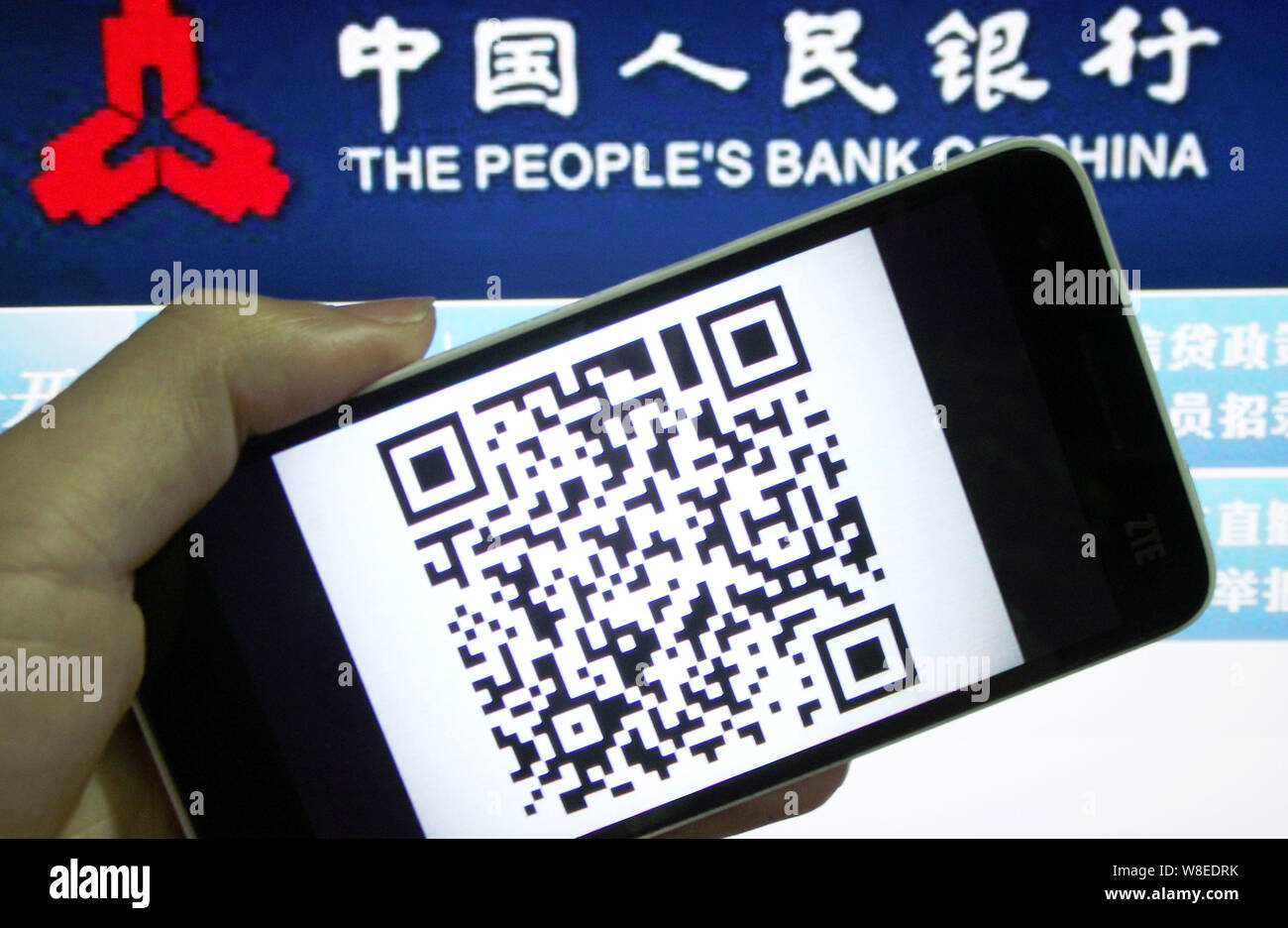 Un chinois d'utilisateurs de téléphones mobiles montre un smartphone affichant un code QR en face d'un logo de la Banque populaire de Chine (PBOC), la banque centrale de Chine, en Banque D'Images