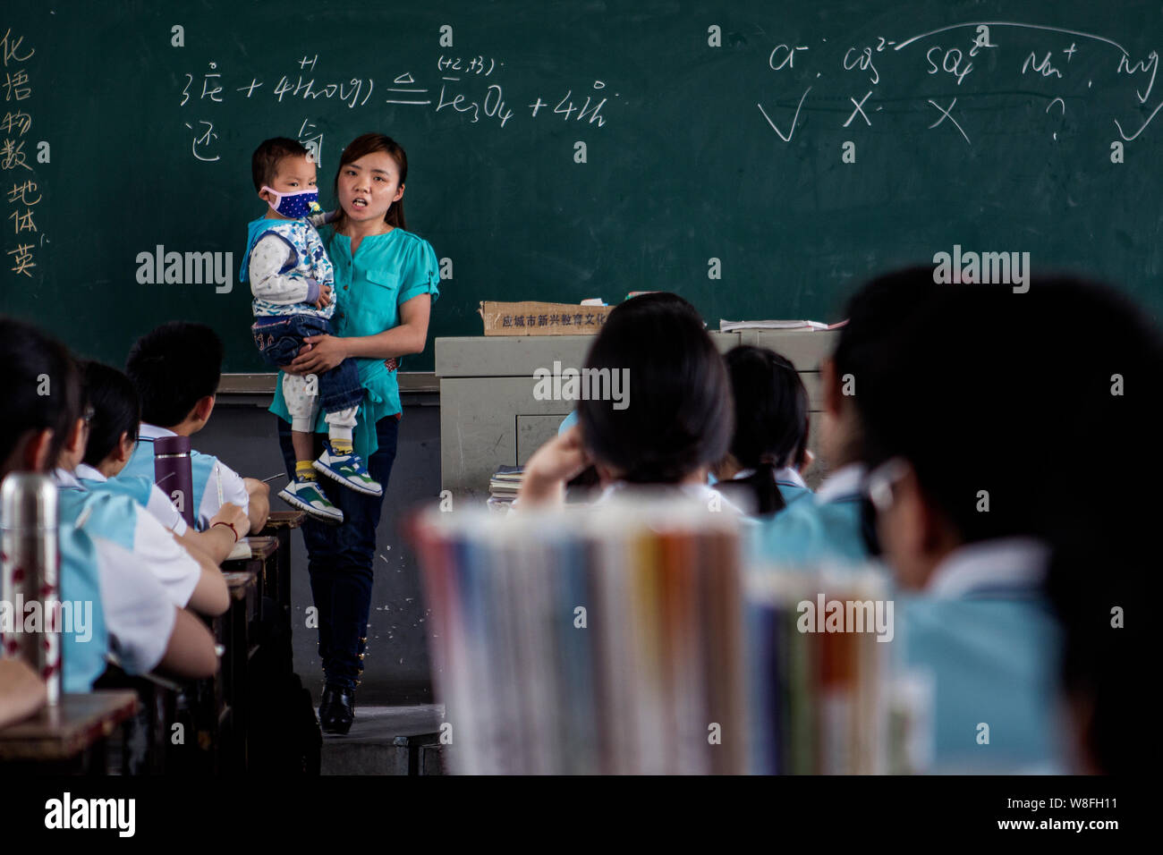 Zhang Wei porte son fils de 3 ans Tutu, qui est atteint de leucémie, tout en donnant une leçon de chimie dans une salle de classe de l'école secondaire n° 1 Hanshou Banque D'Images