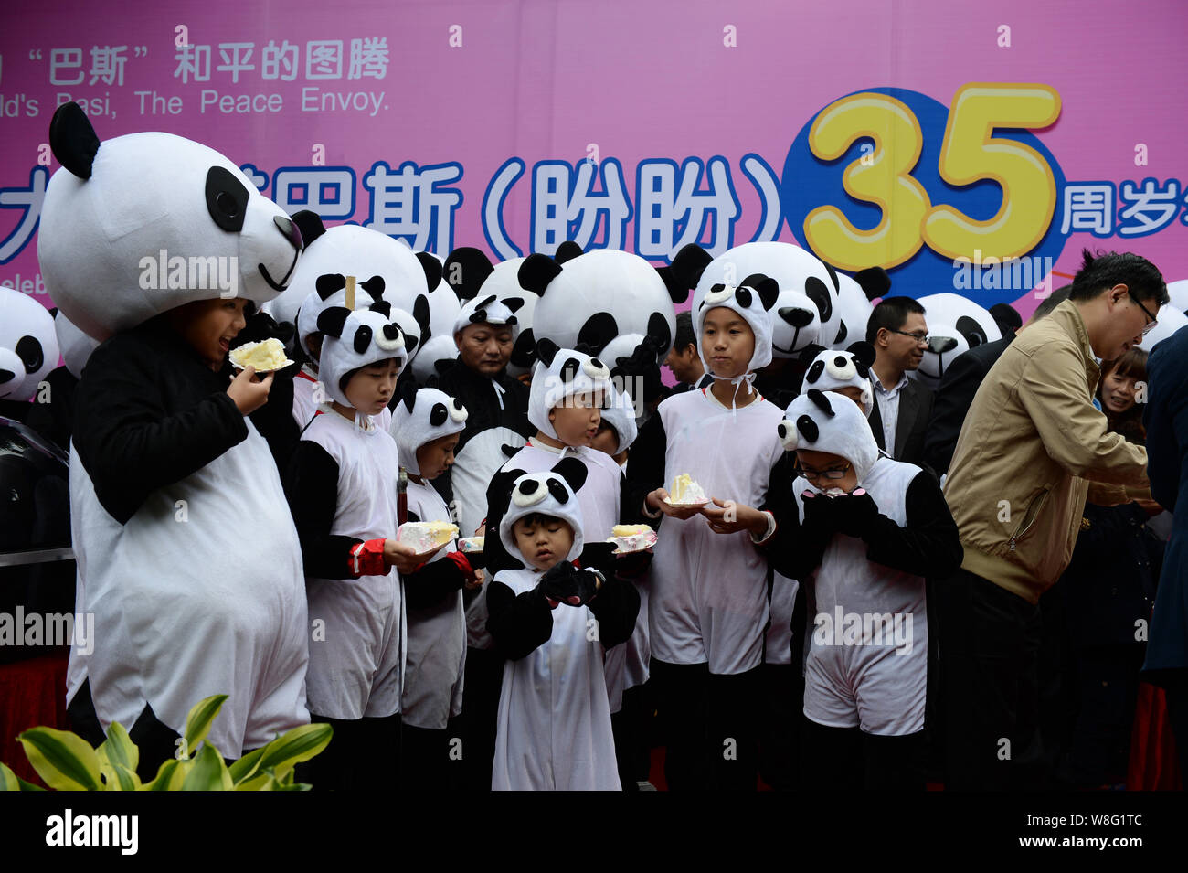 Les enfants vêtus de costumes du panda géant manger des gâteaux pendant une fête pour célébrer le panda géant femelle Basi's 35ème anniversaire au Shanghai Grand Panda recher Banque D'Images
