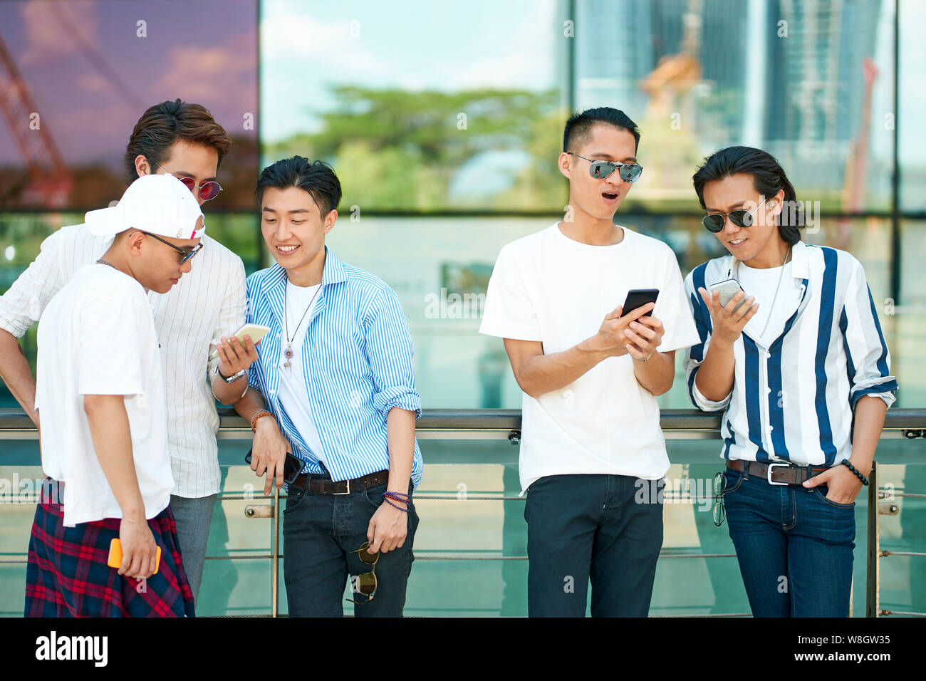 Les jeunes hommes adultes asiatiques utilisent les médias sociaux looking at mobile phone ensemble Banque D'Images