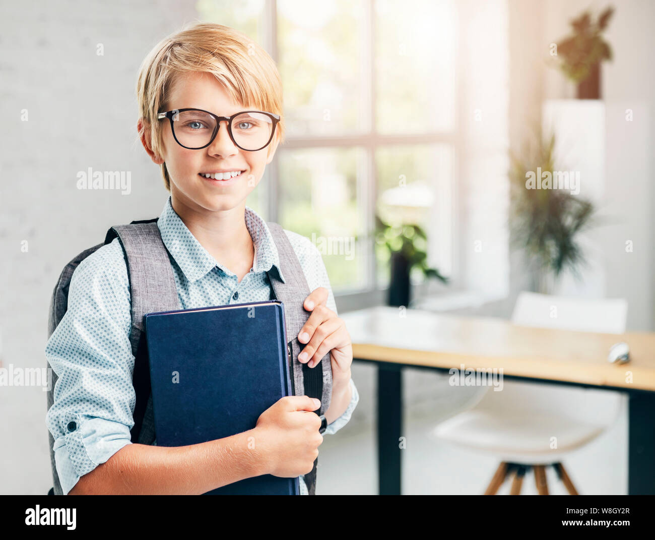Smiling blonde kid avec les manuels scolaires dans une classe Banque D'Images