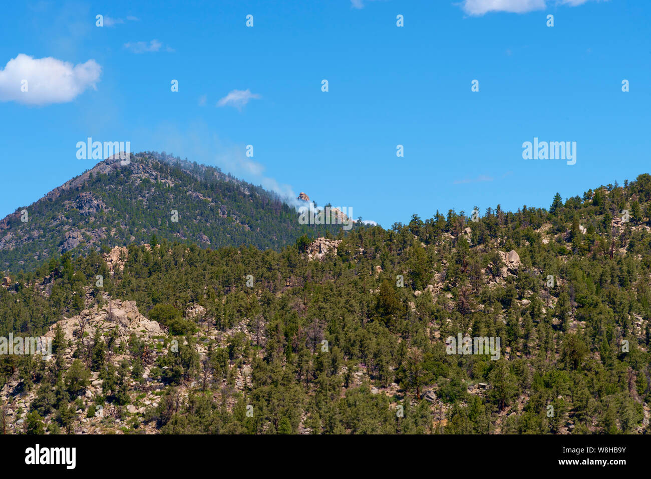 Les montagnes de la Sierra Nevada avec fumée blanche à l'incendie de forêt près de pic en vertu de ciel bleu avec des nuages blancs. Banque D'Images Les montagnes de la Sierra Nevada avec fumée blanche à l'incendie de forêt près de pic en vertu de ciel bleu avec des nuages blancs. Banque D'Images