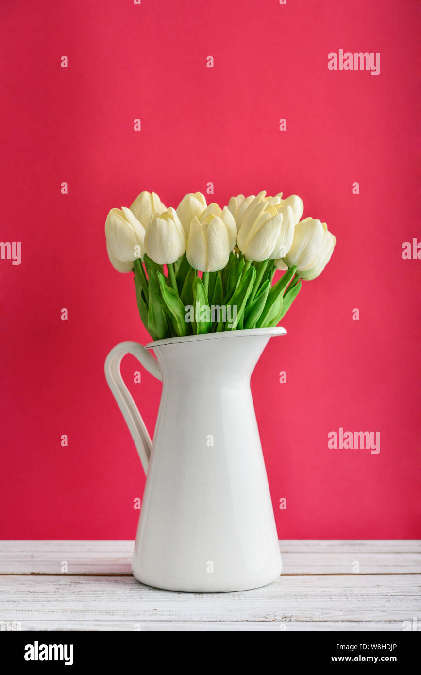 Bouquet de tulipes blanches en pot émaillé blanc sur fond rose Banque D'Images
