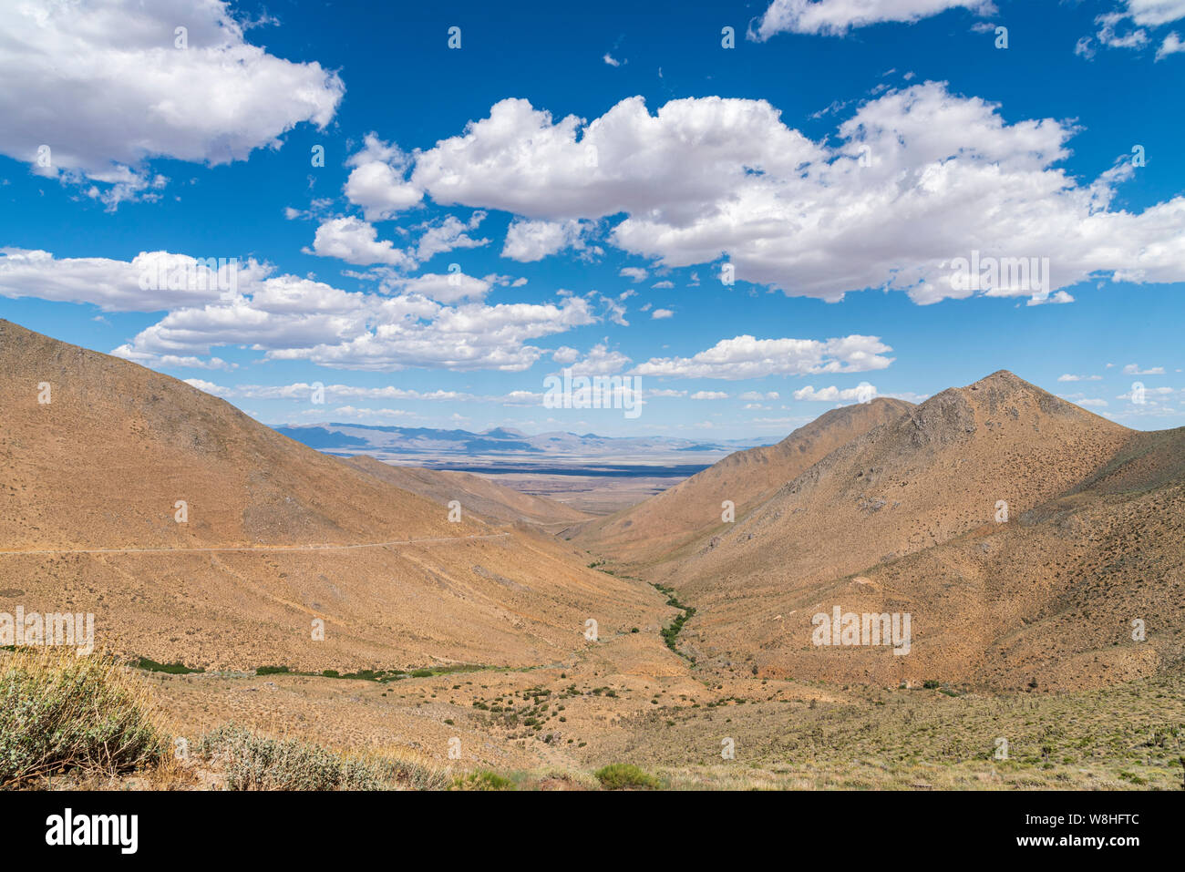 Montagnes arides brown avec peu de végétation sous ciel bleu avec des nuages blancs moelleux. Desert canyon avec vallée au-delà. Banque D'Images