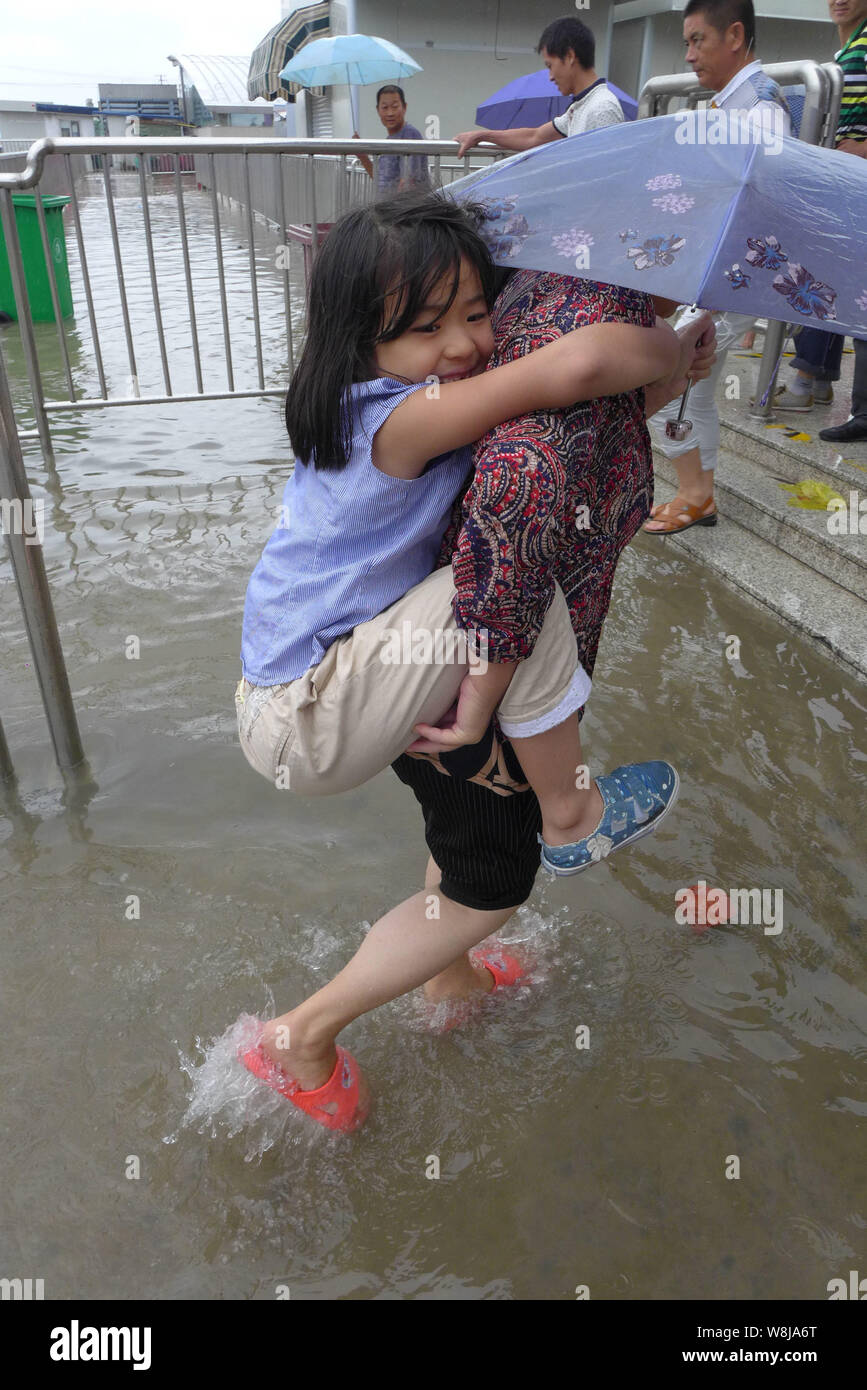 Une femme portant sa fille marche sur une route inondée dans une forte pluie causés par le typhon Goni à Shanghai, Chine, 24 août 2015. Shanghai est devenue Banque D'Images