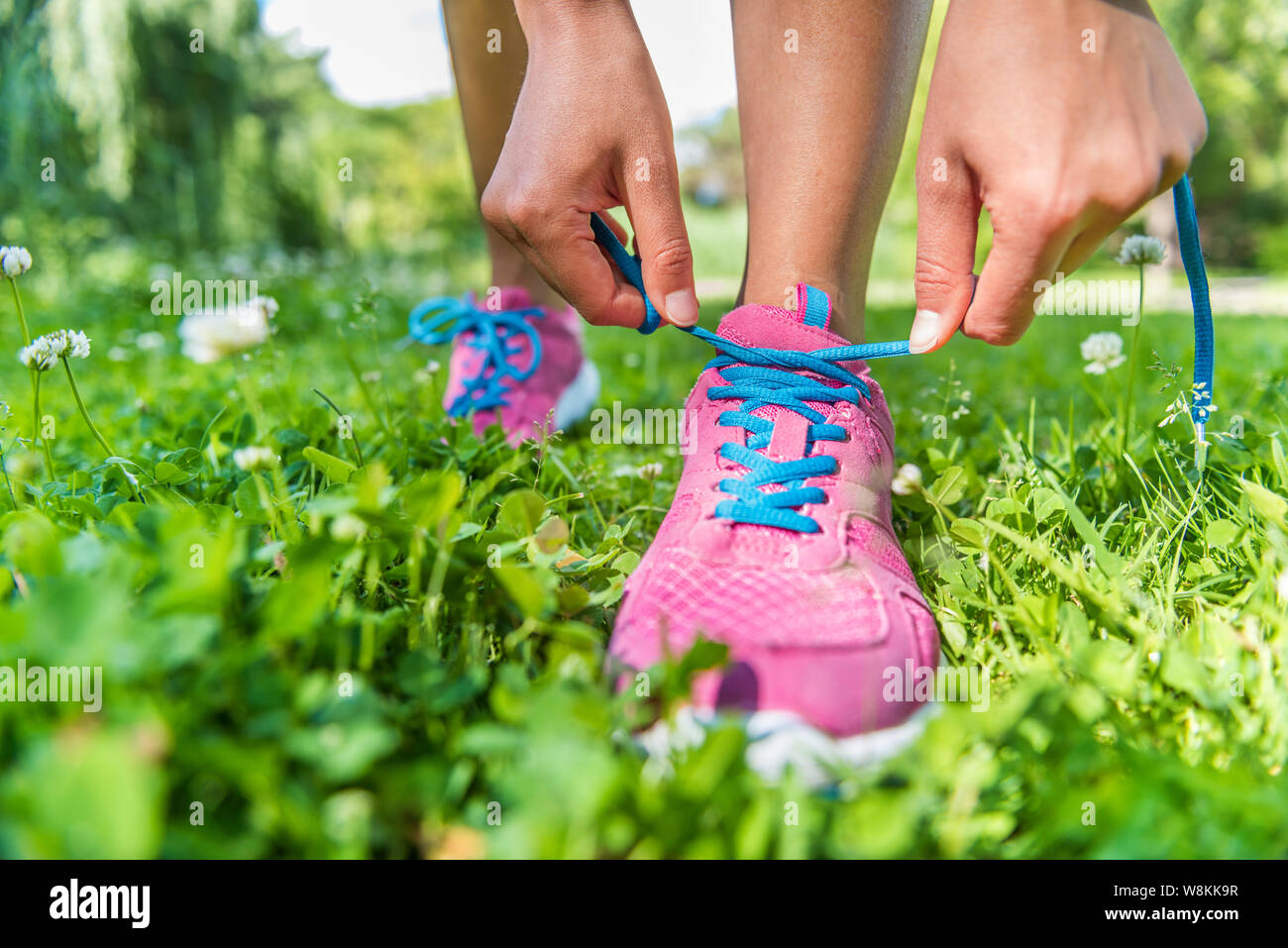 Vie active saine athlète attachant des chaussures de course. Happy sporty girl runner lacets laçage sur rose fashion sneakers sur l'herbe d'été dans le parc de la ville se préparer pour un footing de remise en forme. Banque D'Images