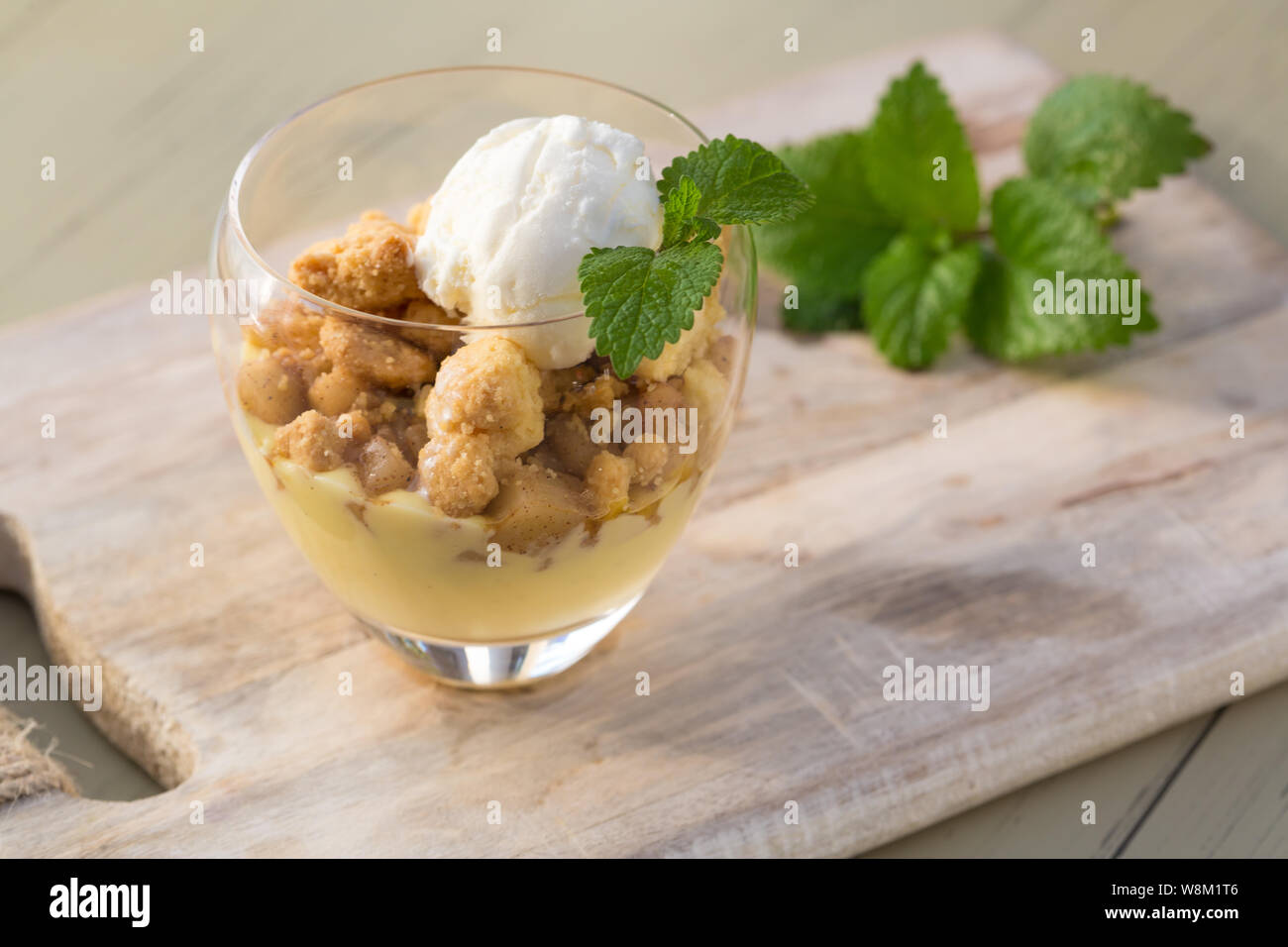 Topping crumble aux pommes glace vanille servie avec melisa en verre et plateau en bois sur la table. Banque D'Images