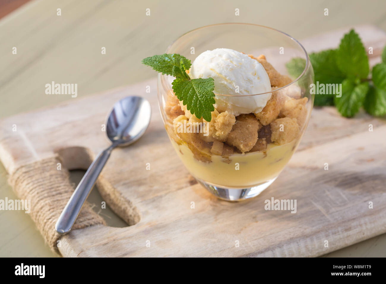 Topping crumble aux pommes glace vanille servie avec melisa en verre et plateau en bois sur la table. Banque D'Images