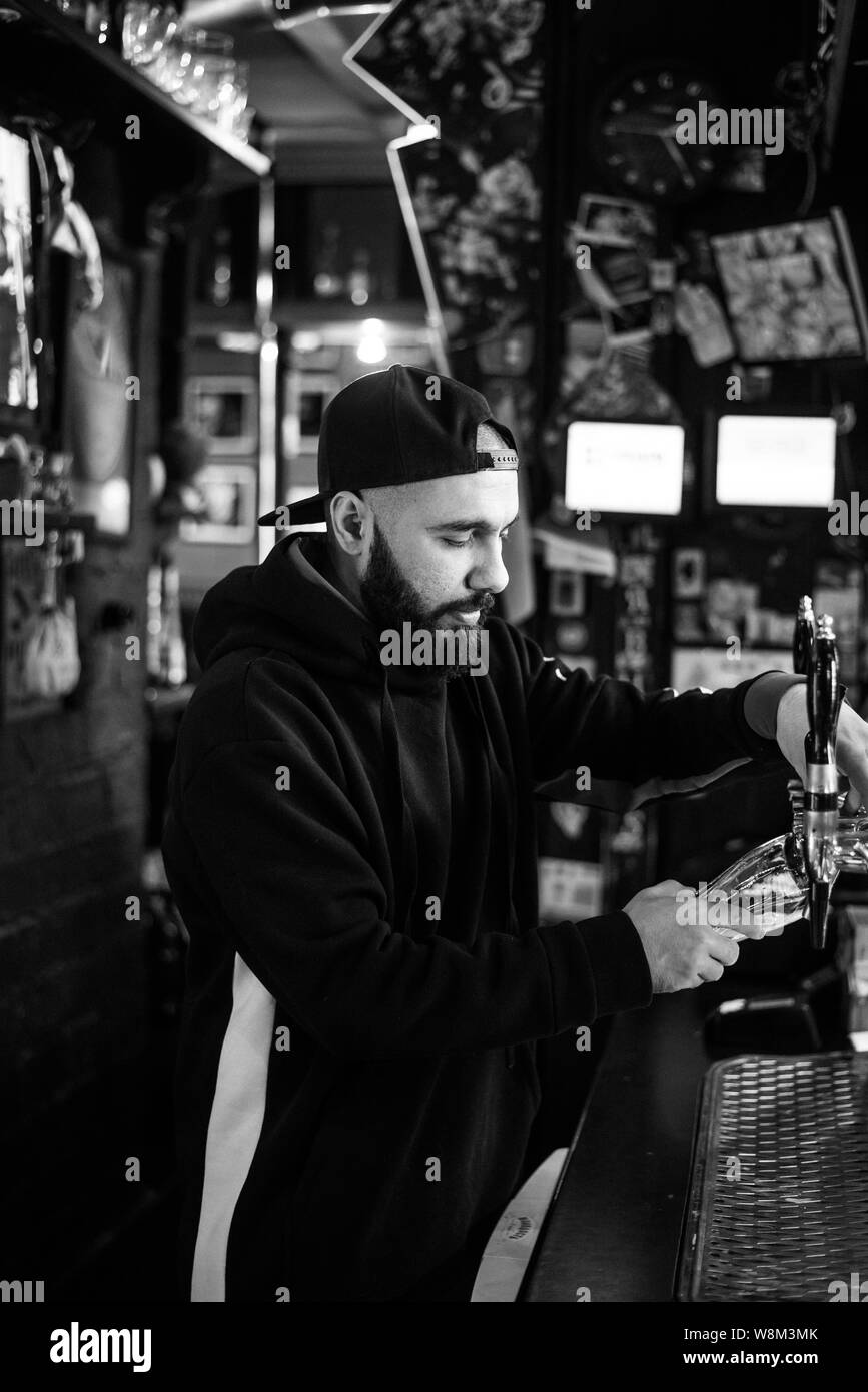 Barman souriant servir la bière dans un bar. Homme courageux barbus vous verse un verre de mousse. Appuyez sur or pour la bière pression. Banque D'Images