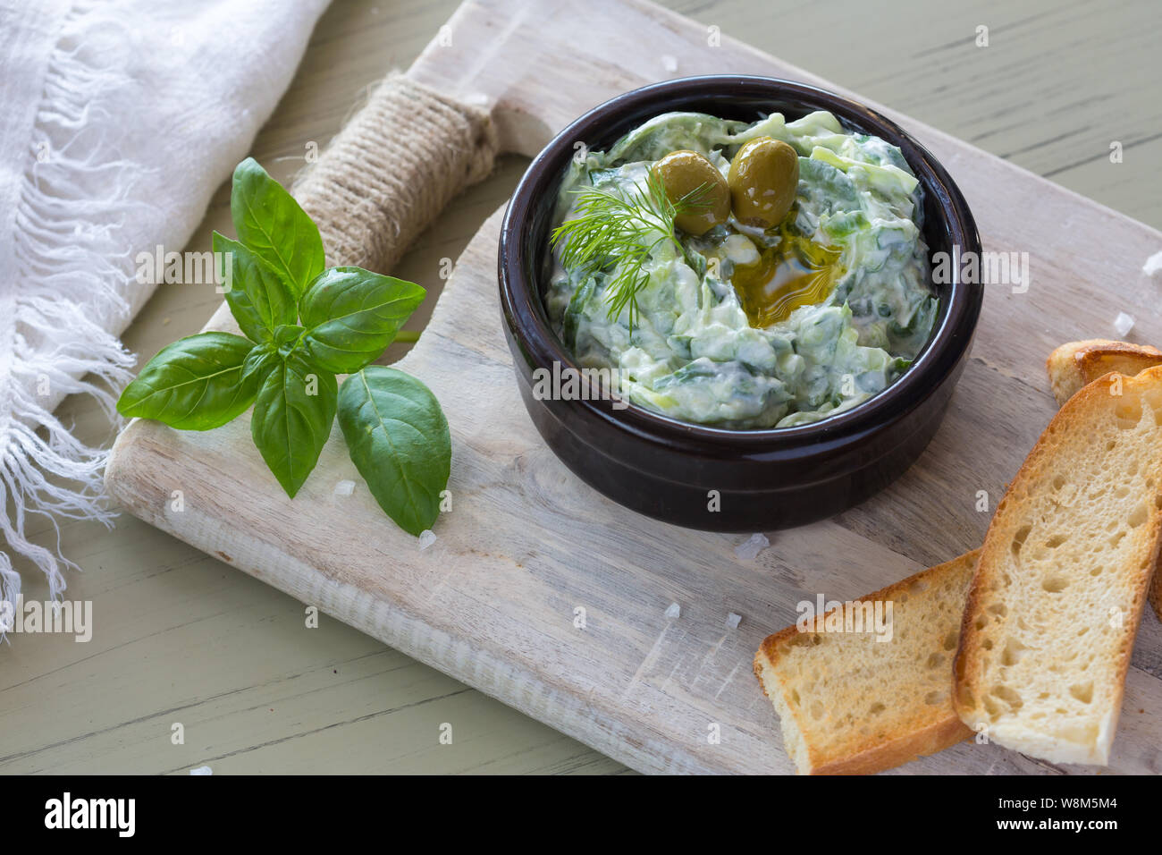 Trempette grecque tzatziki sauce ou vinaigrette ingrédients et décoré avec de l'huile d'olive et basilic sur table en bois Banque D'Images