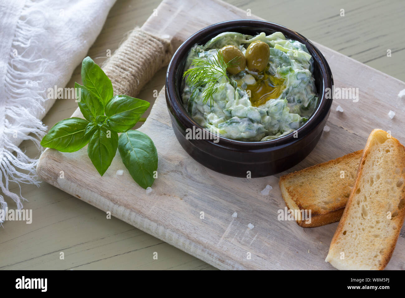 Trempette grecque tzatziki sauce ou vinaigrette ingrédients et décoré avec de l'huile d'olive et basilic sur table en bois Banque D'Images