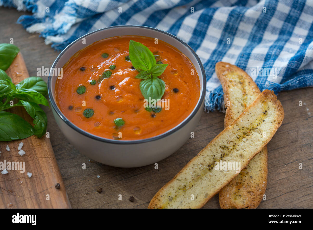 Un bol de soupe aux tomates fraîches en white Ceramic Bowl, garnie de croûtons, de basilic, de l'expérience et un filet d'huile d'olive et servi avec du pain croustillant. Banque D'Images