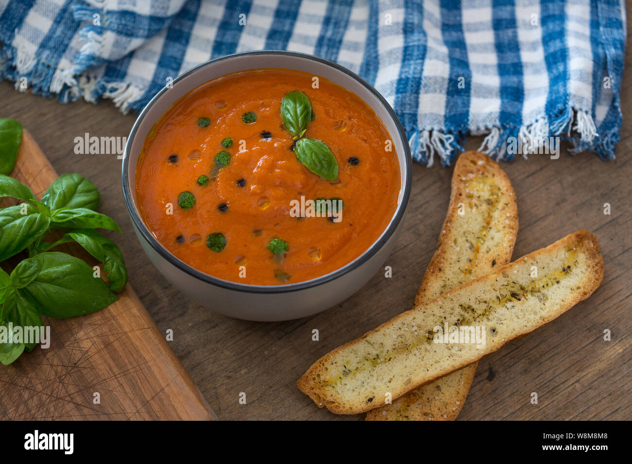 Un bol de soupe aux tomates fraîches en white Ceramic Bowl, garnie de croûtons, de basilic, de l'expérience et un filet d'huile d'olive et servi avec du pain croustillant. Banque D'Images