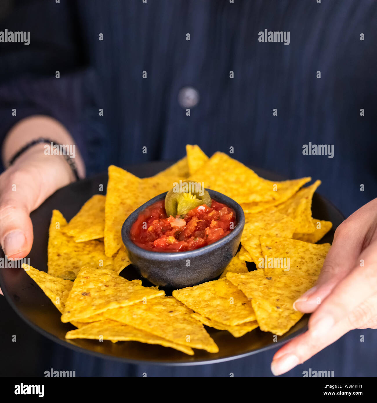 Mains tenant la plaque avec nachos mexicain et sauce chili rouge.Lifetyle Street food contexte . Banque D'Images