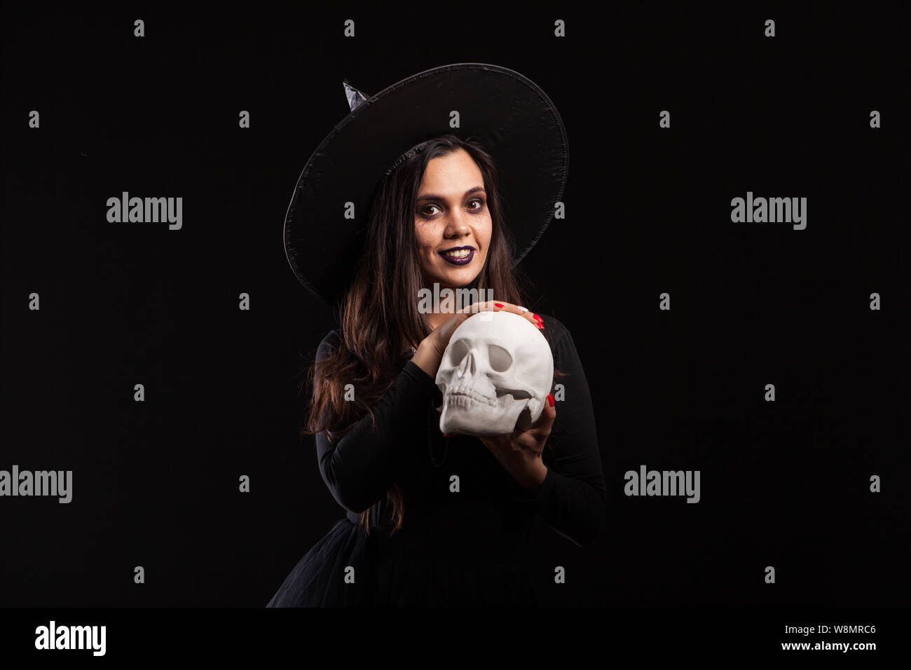 Jolie jeune femme dans un costume de sorcière pour Halloween party faisant le mal la sorcellerie. Portrait de femme magic sur un crâne humain. Banque D'Images