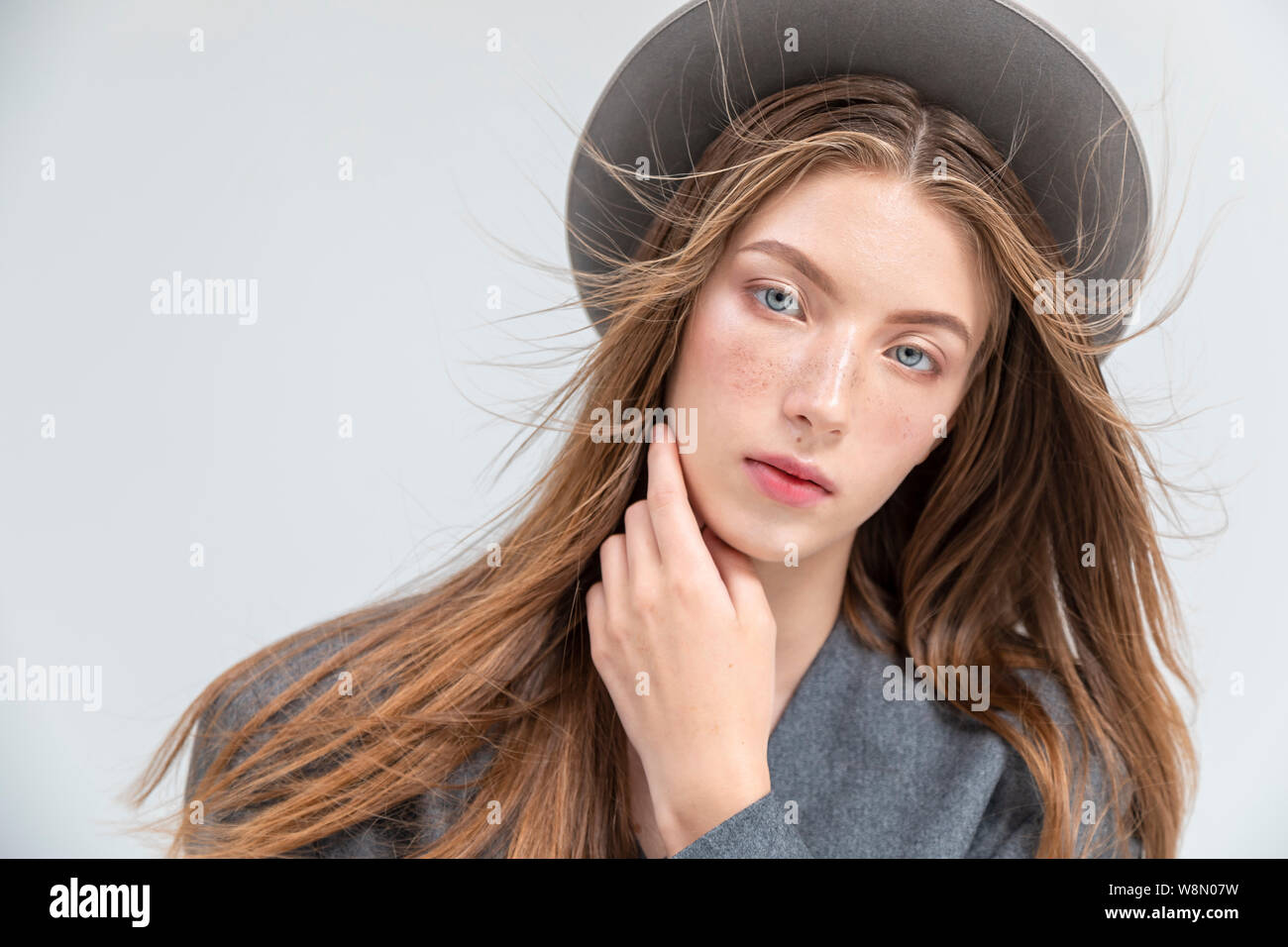 Portrait d'une jeune femme en gris à la caméra en se frottant le menton isolé sur fond blanc copyspace Banque D'Images