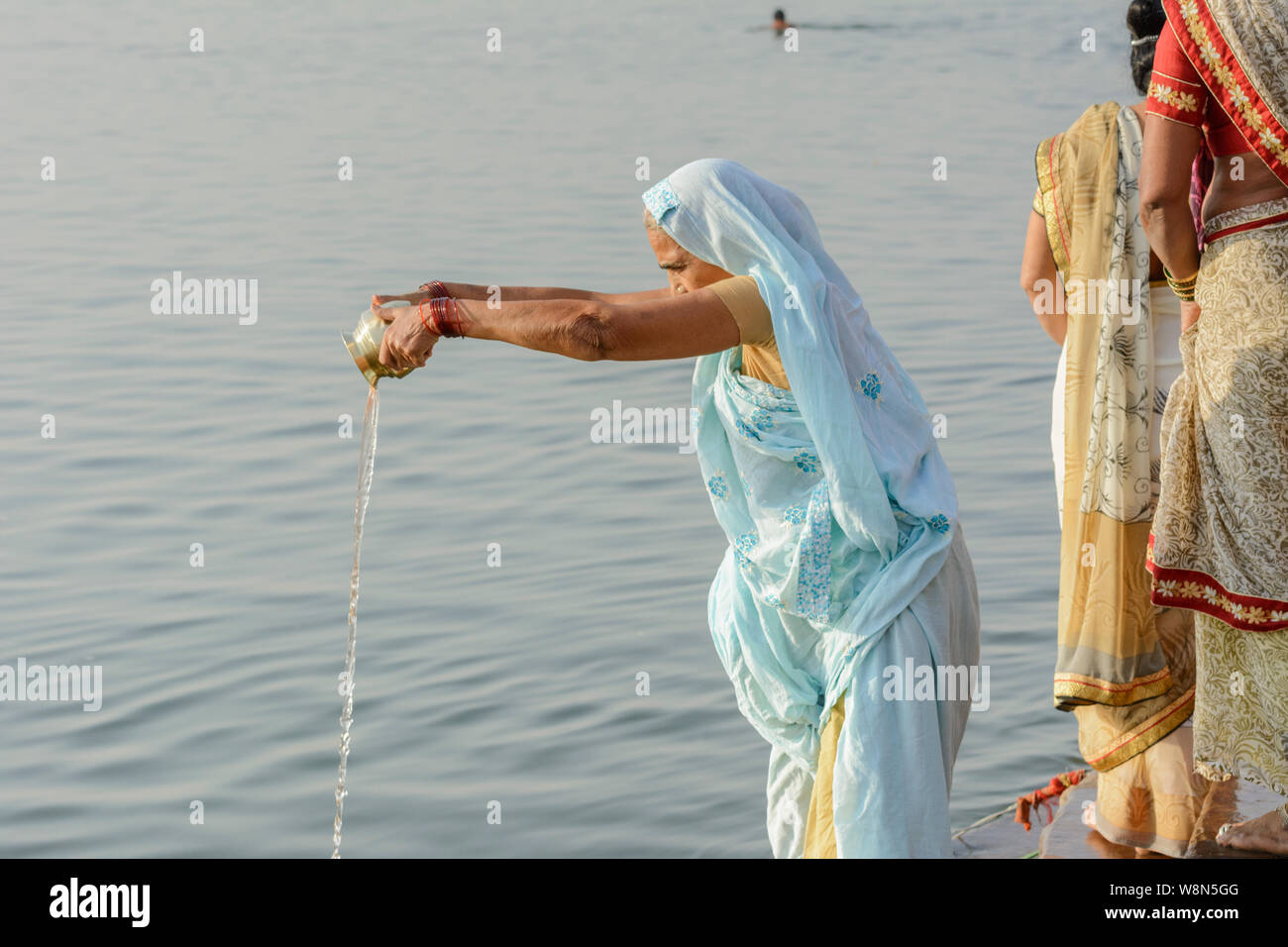 Une vieille femme hindoue indienne dans un sari verse des offrandes aux dieux (libations) dans le Gange à Varanasi, Uttar Pradesh, Inde, Asie du Sud. Banque D'Images