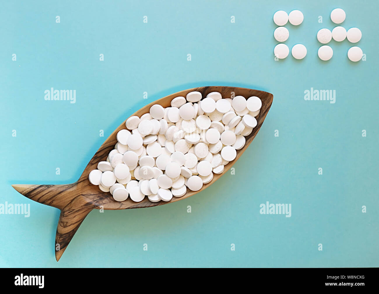 Comprimés de calcium dans un plat en bois sous la forme d'un poisson. Le  poisson est riche en calcium. Arrière-plan de couleur. Parole de CA (calcium)  est définie par des pilules. Flay