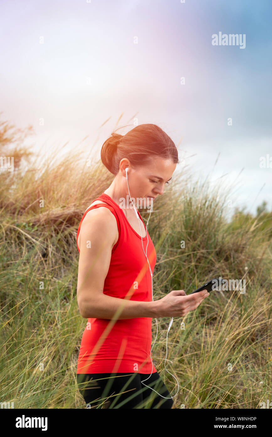 Femme avec casque, écouteurs, contrôler son téléphone portable après l'exercice à l'extérieur Banque D'Images