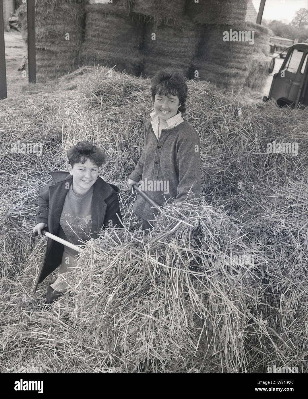 Années 1980, historiques, deux adolescentes qui travaillent dans une grange à foin, pendant les vacances d'été, England, UK. Banque D'Images