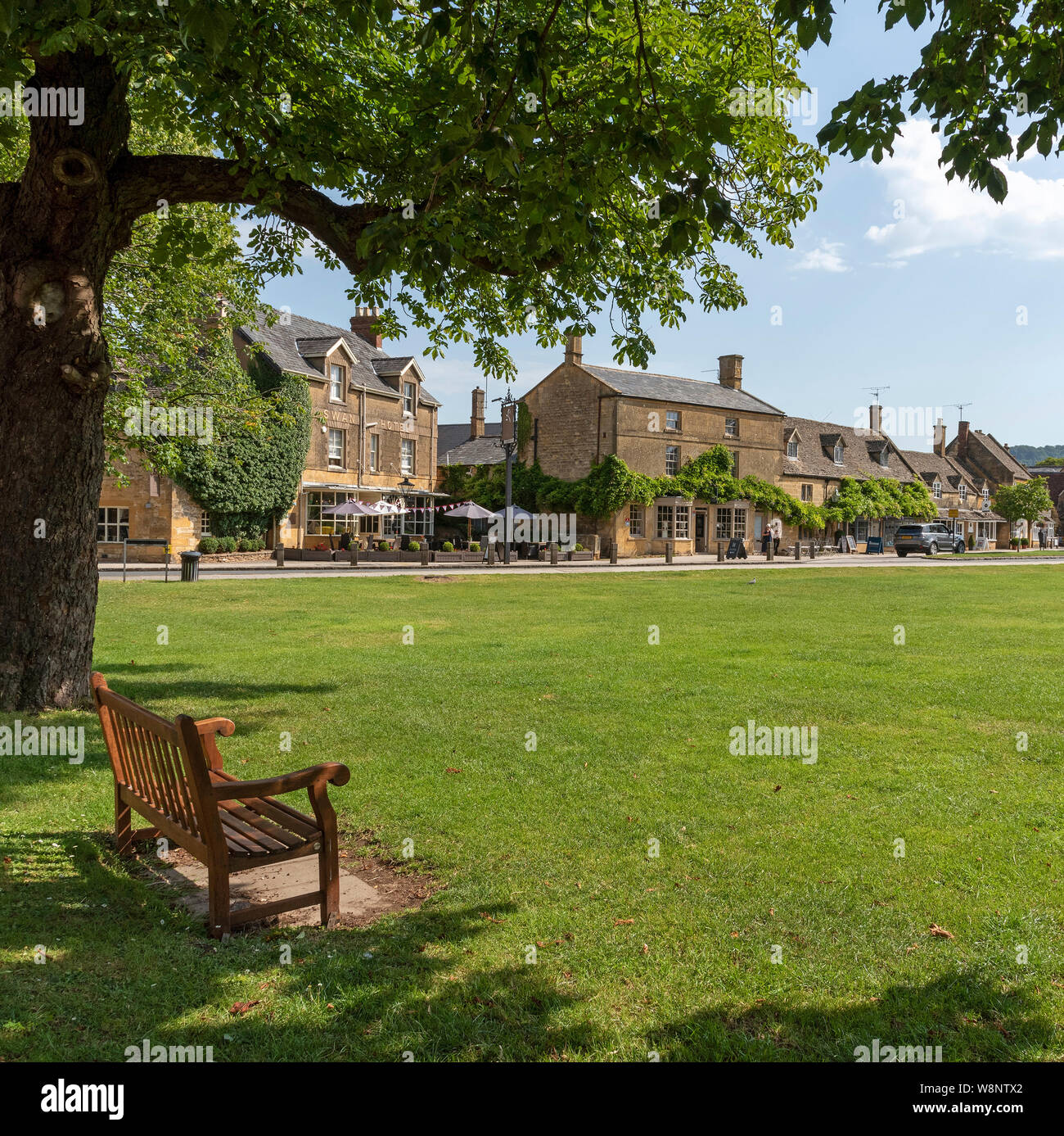 Broadway, Worcestershire, Angleterre, Royaume-Uni. Une assise en bois sur le bord du livre vert au centre du village bordée de bâtiments en pierre calcaire de couleur miel. Banque D'Images