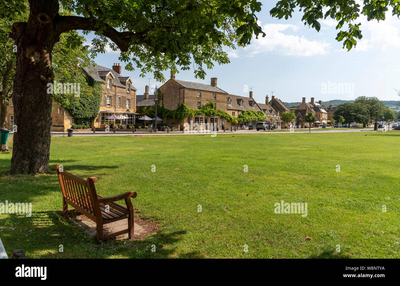 Broadway, Worcestershire, Angleterre, Royaume-Uni. Une assise en bois sur le bord du livre vert au centre du village bordée de bâtiments en pierre calcaire de couleur miel. Banque D'Images