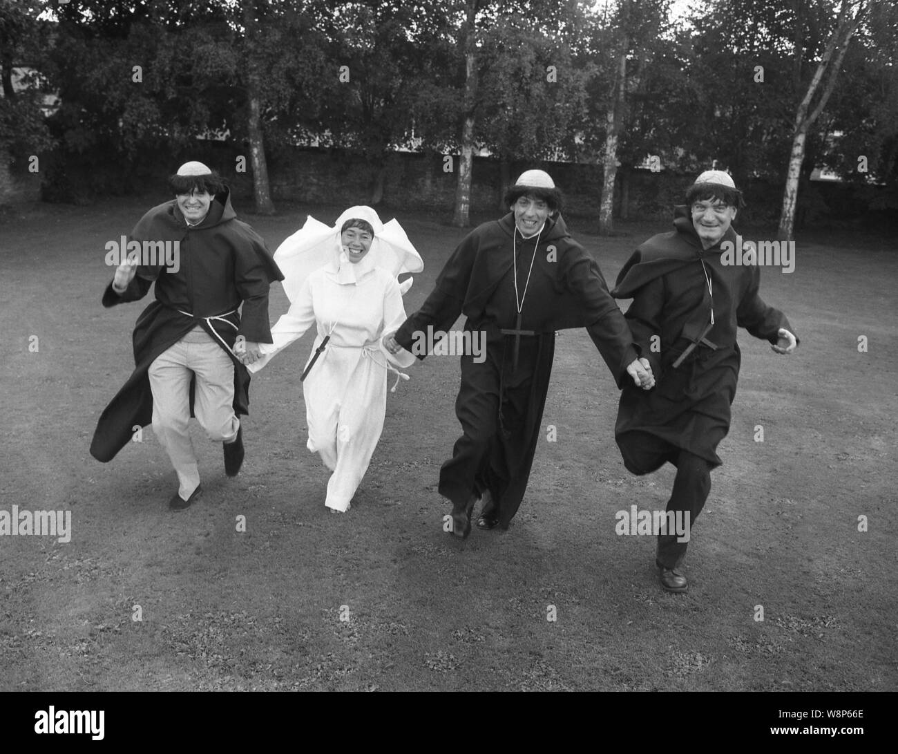 Années 1980, historique, les hommes et les femmes habillés en robe, comme frères et une religieuse, tournant en extérieur dans un fieldEngland, UK. Banque D'Images