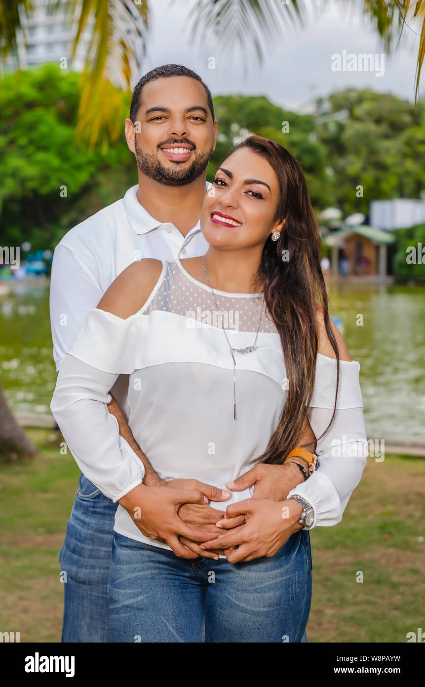 Couple de jeunes hommes et femmes d'Amérique latine et heureux à l'extérieur en portrait, ensemble dans un parc, ju à la fois rire et romantique hugging Banque D'Images