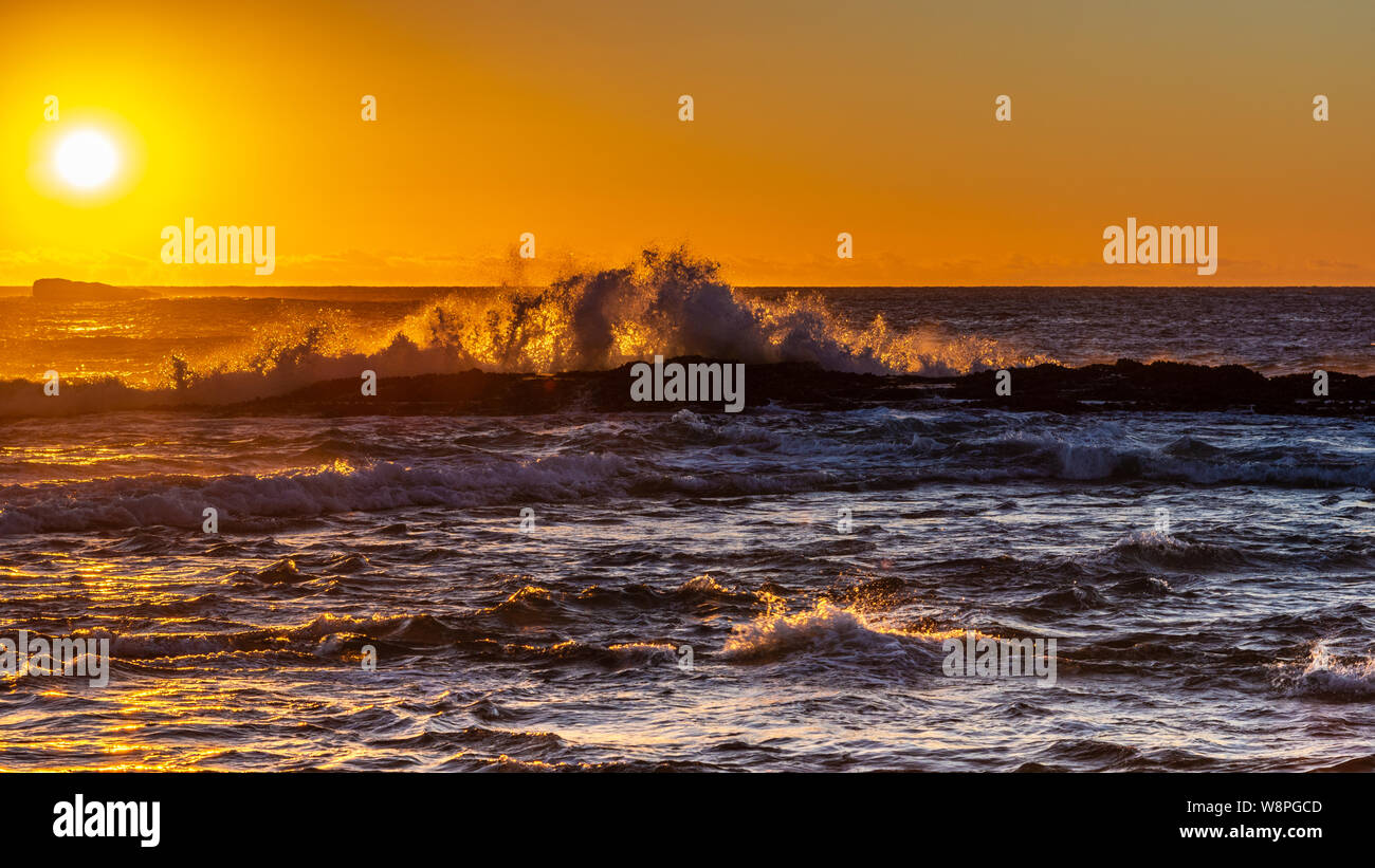 Lever du soleil sur l'océan avec des vagues se brisant sur les roches Banque D'Images