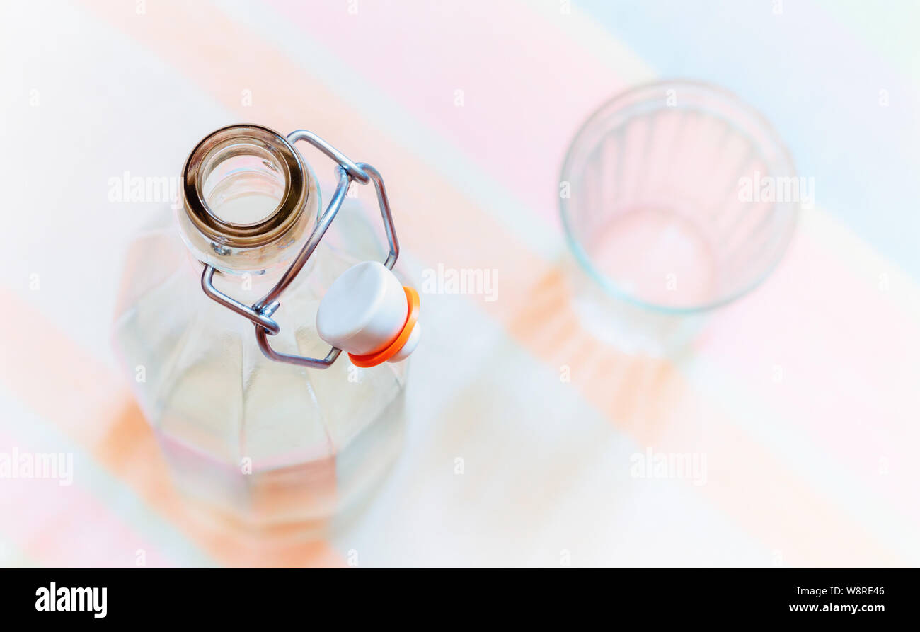 Vue de dessus une bouteille en verre avec un fil crochet de bouchon en céramique, et d'un verre, sur un bleu, rose et orange nappe dénudée Banque D'Images