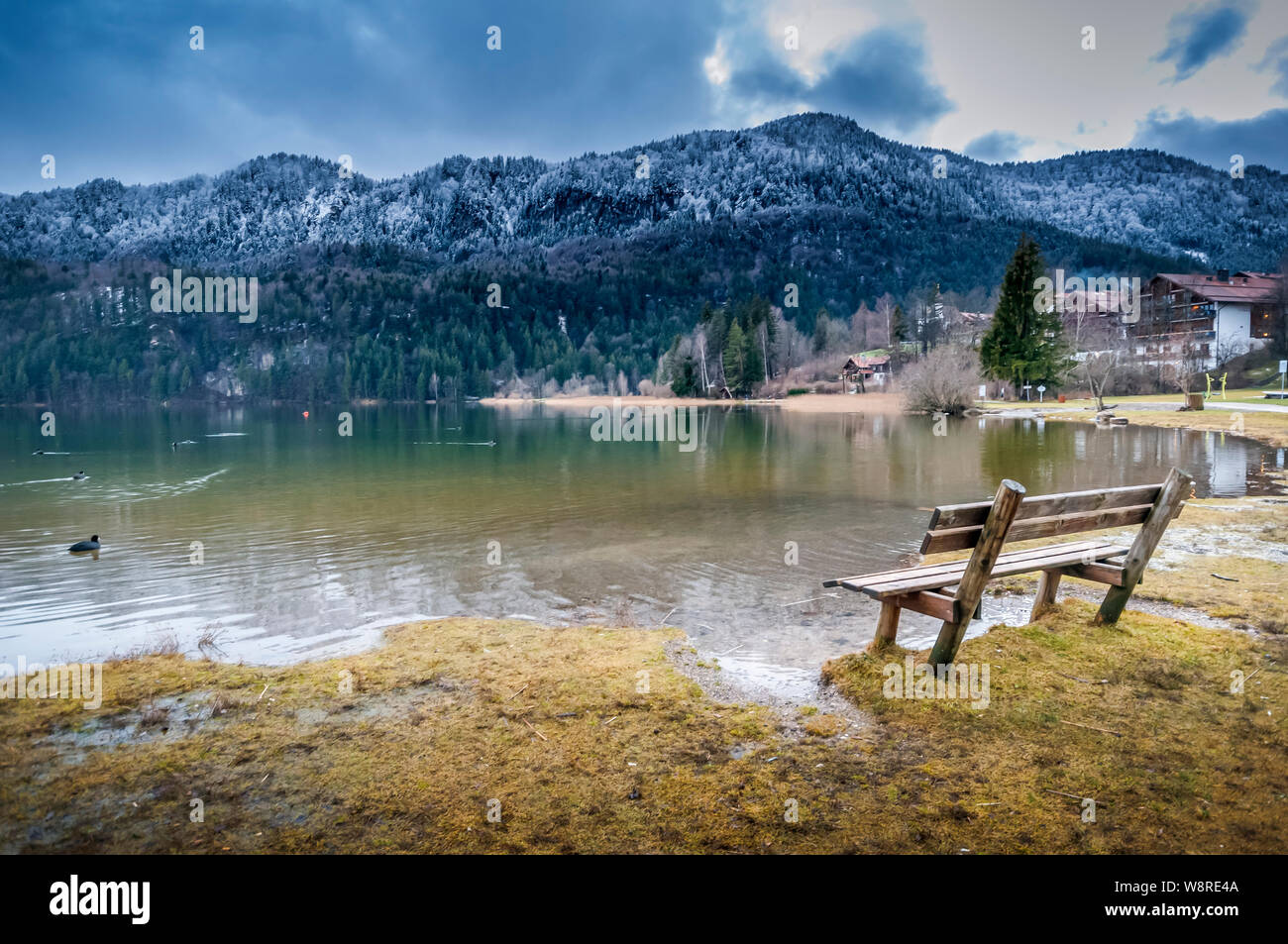 Seul banc en bois à Weissensee avec couverts de givre hiver forêt de montagne dans l'arrière-plan. Banque D'Images