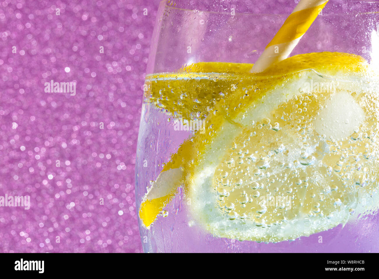 Des bulles de soude avec un cube de glace, d'une tranche de citron et une paille sur un fond rose. Espace libre pour le texte Banque D'Images