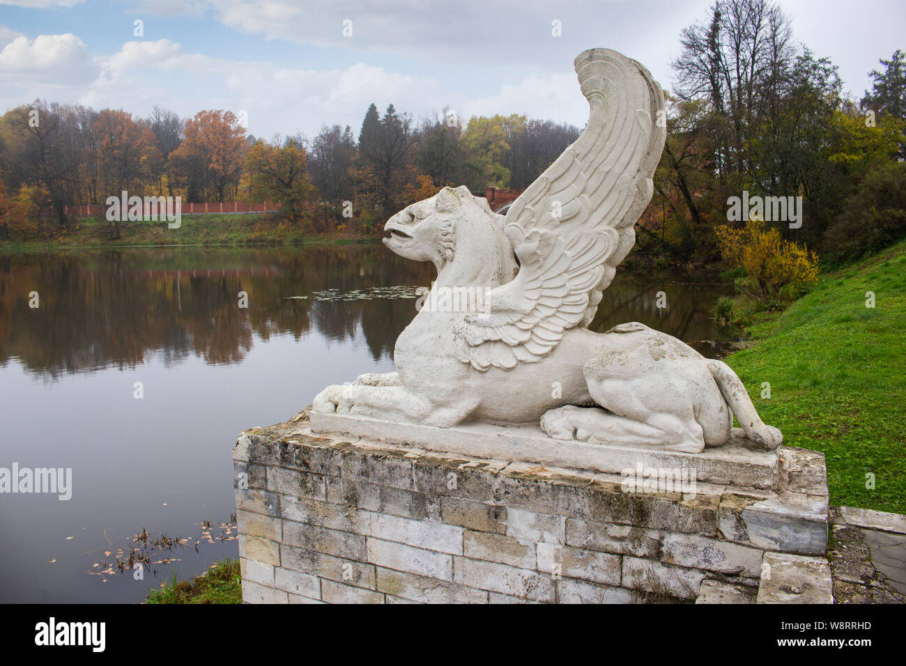 Pierre béton lion avec des ailes de la statue, la gargouille sur le socle en pierre, décoration de la Manor Park, la rive de l'étang du lac automne paysag Banque D'Images