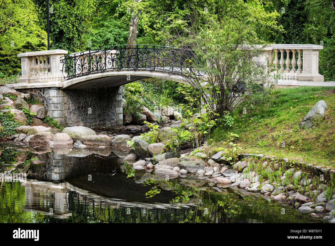 Pont de style classique sur un canal par le lac en paysage tranquille du parc Château Ujazdowski à Varsovie, Pologne. Banque D'Images