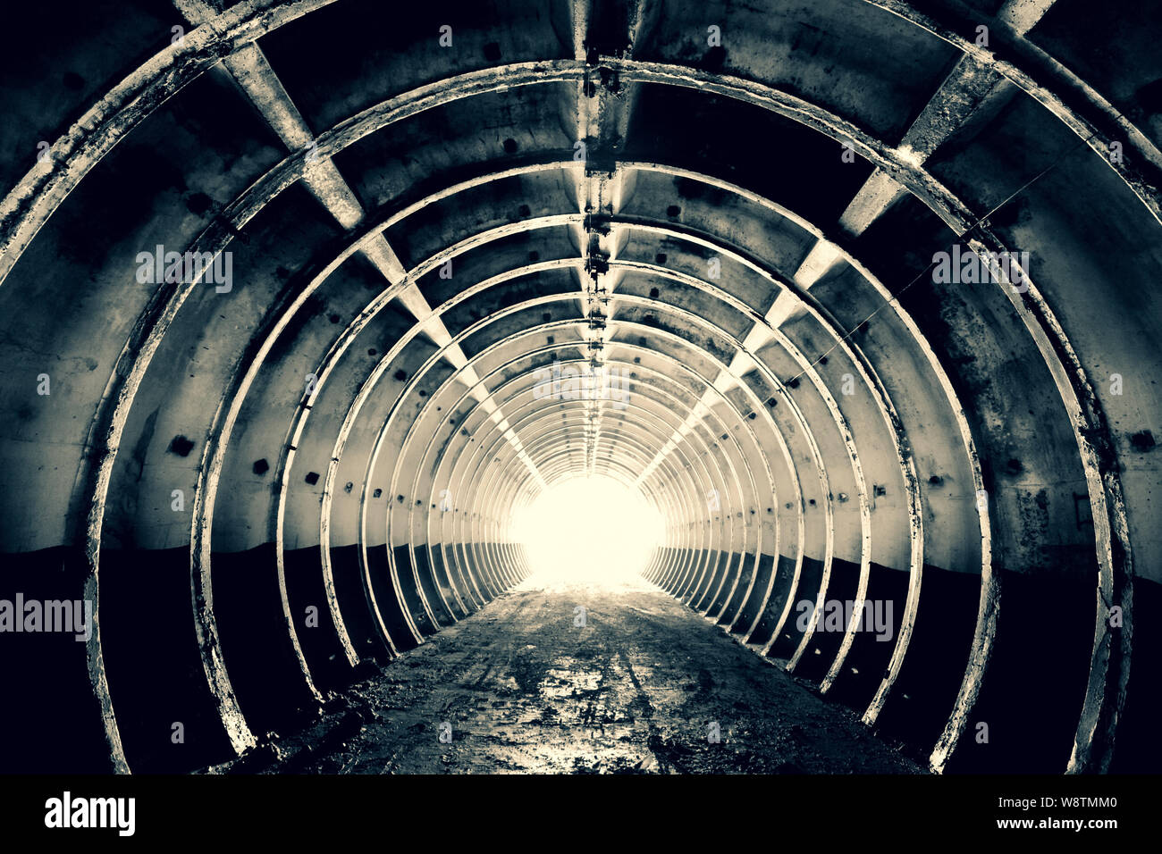 L'abstraction de l'arrière-plan. Tunnel avec nervures rigides annulaire et une lumière vive à la fin de la construction militaire concret. Noir et blanc. Teintées. Banque D'Images
