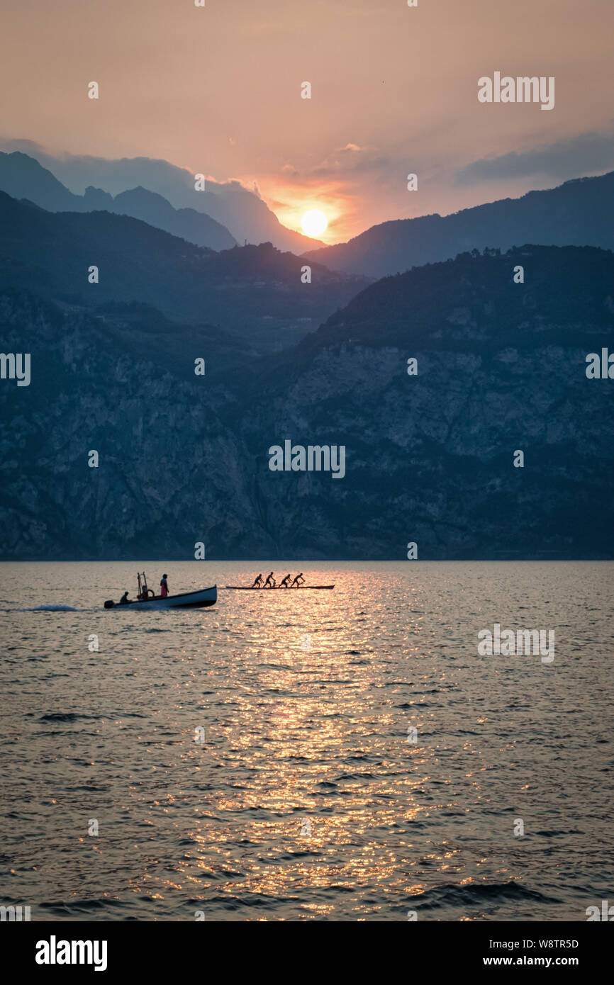Il s'agit d'un coucher du soleil photo du Lac de Garde. Int le premier plan il y a un bateau de pêche et une équipe d'aviron. Dans l'arrière-plan est le soleil derrière le Banque D'Images