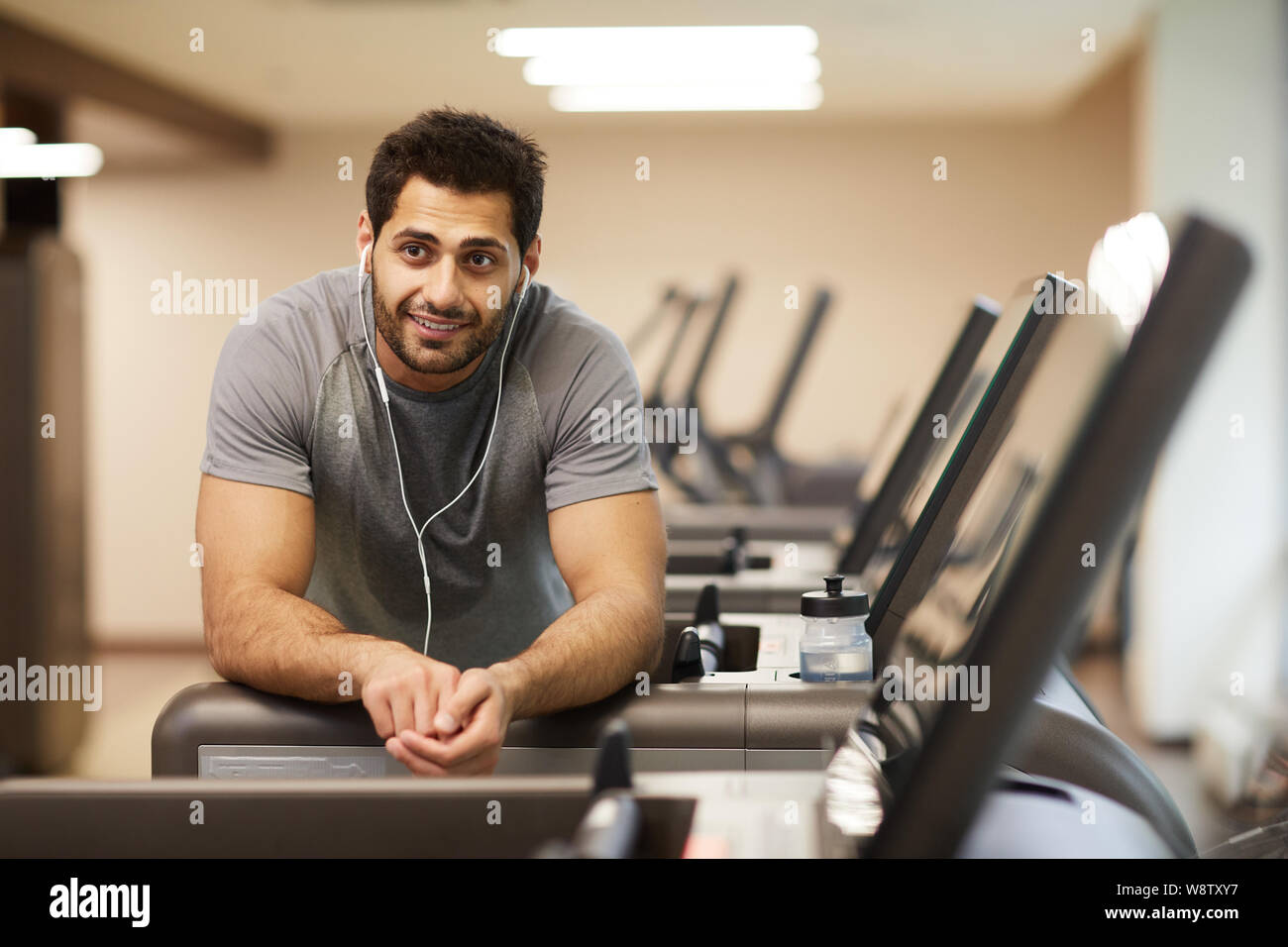 Portrait de l'homme musclé en pause de l'exercice dans la salle de sport et à l'écoute de musique, copy space Banque D'Images