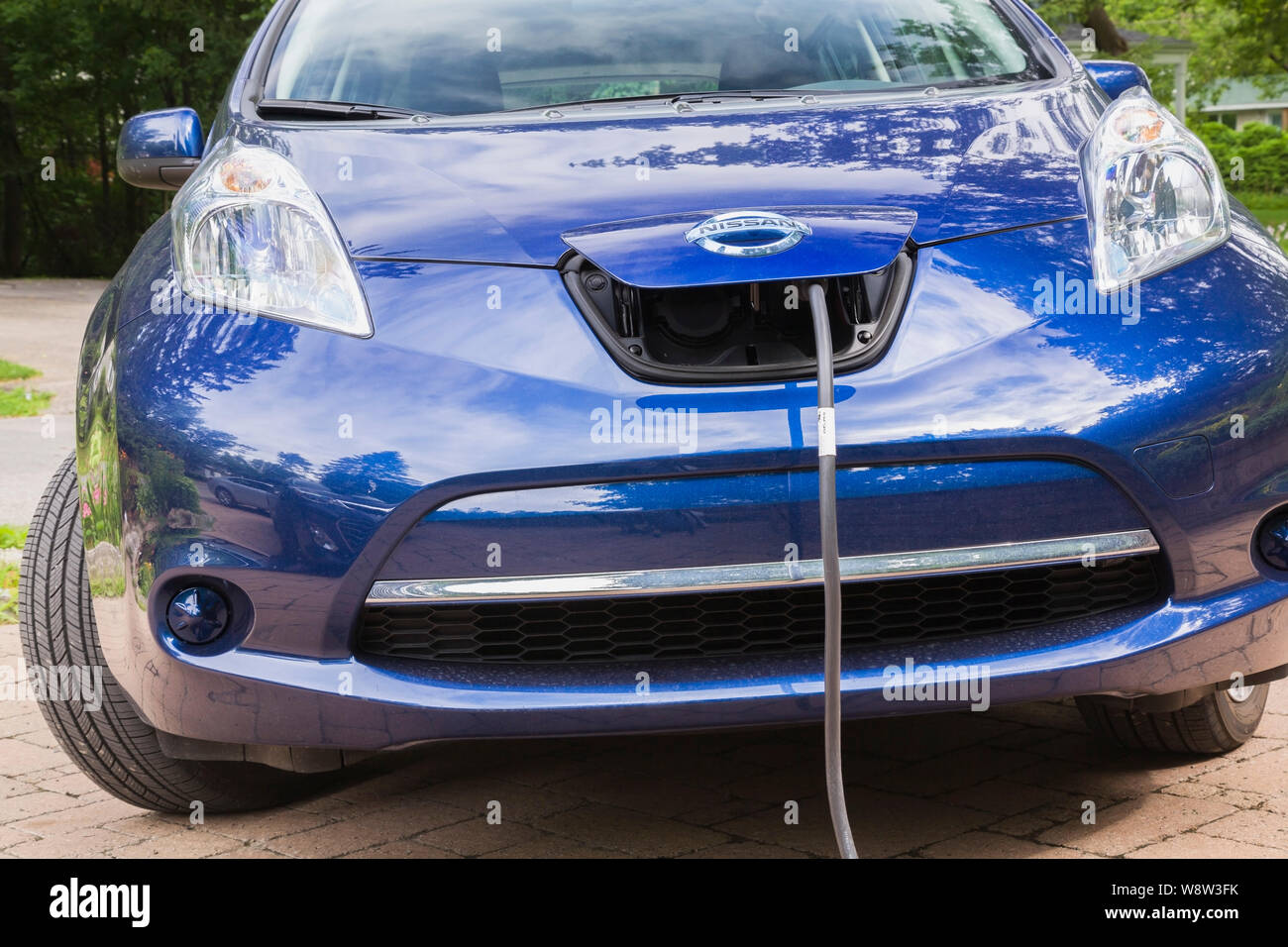 Voiture électrique Nissan bleu avec le connecteur branché et de charge en entrée en face de l'immeuble d'accueil Banque D'Images