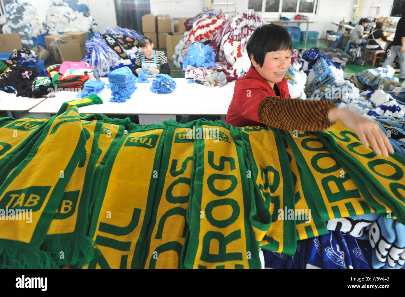 Une femme travailleur chinois examine les écharpes de ventilateur du Brésil et l'Australie (maillots de football national) produits pour le monde Brésil 2014 Banque D'Images