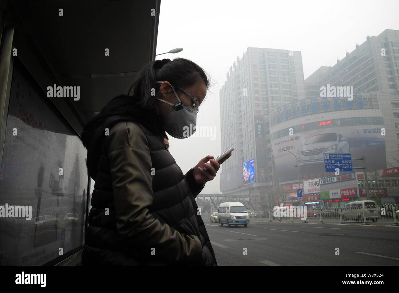 Un passager portant un masque de visage utilise son téléphone portable à une station de bus dans le smog lourde à Beijing, Chine, 27 mars 2014. Le smog épais a continué d'affec Banque D'Images