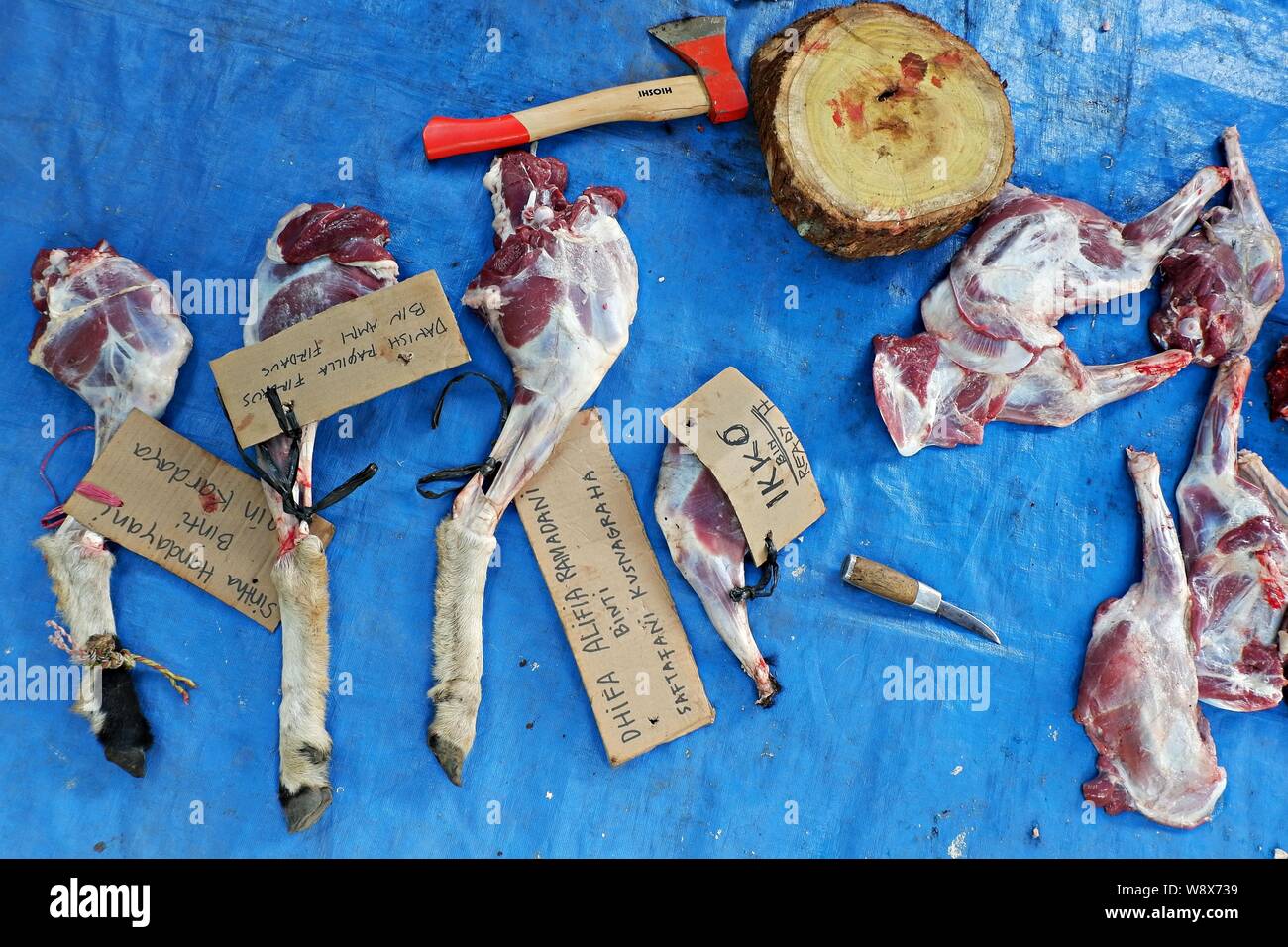 Quelques pattes d'agneau pelées attachées au papier avec des noms écrits à côté d'une hache de boucherie et d'un tableau de découpe en bois. Banque D'Images