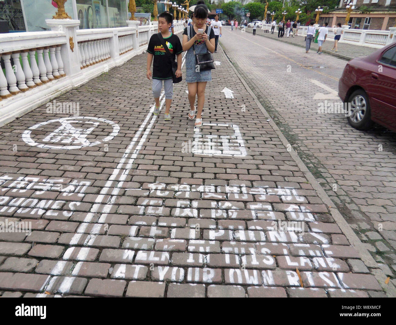 Un piéton utilise son portable qu'elle marche sur le trottoir de téléphone mobile à Chongqing, Chine, le 13 septembre 2014. À gauche, les gens se concentrer sur Banque D'Images