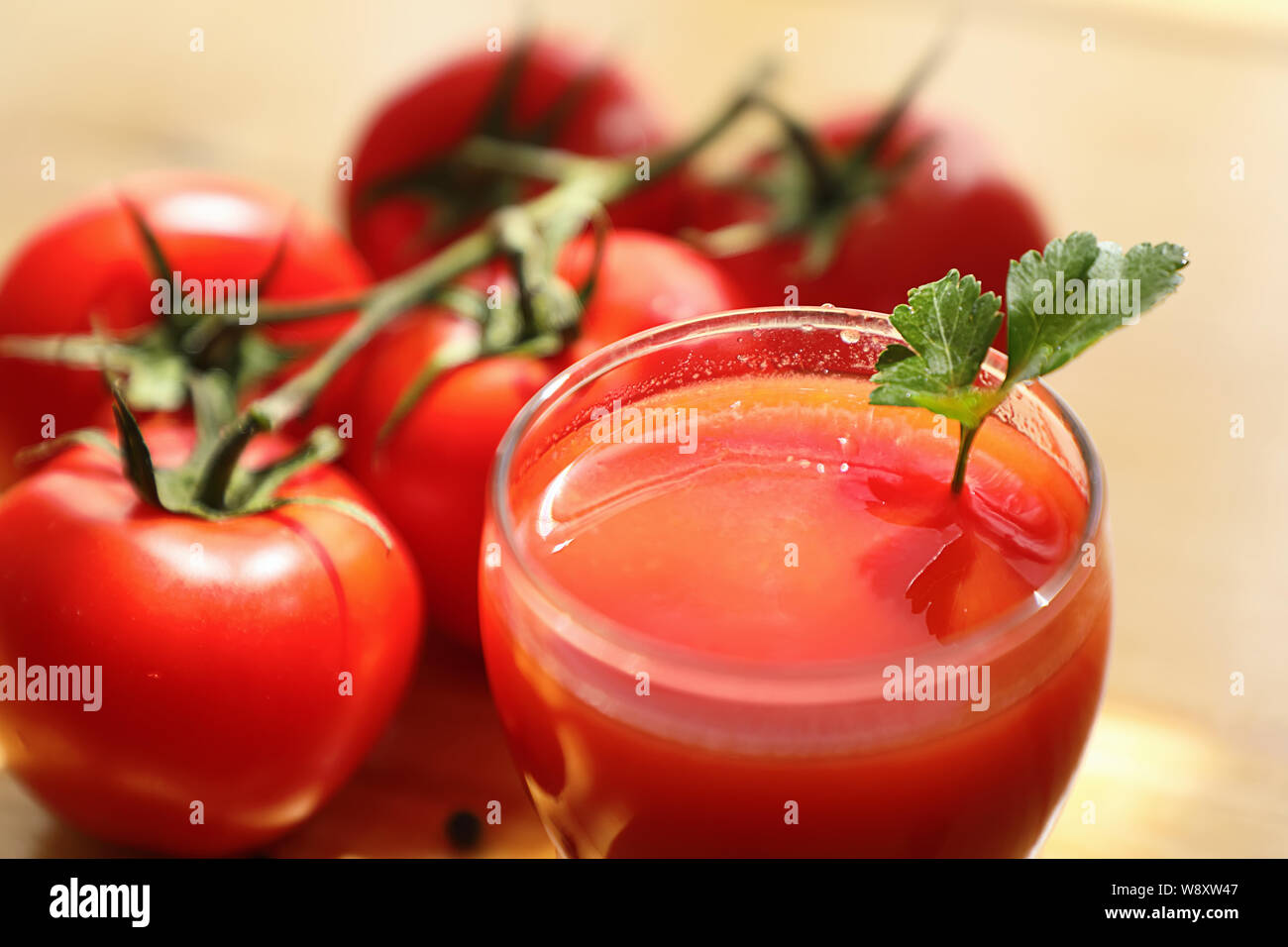 Du jus de tomate dans une tasse en verre avec un tas de tomates mûres, sur un fond en bois clair. Close up. Banque D'Images